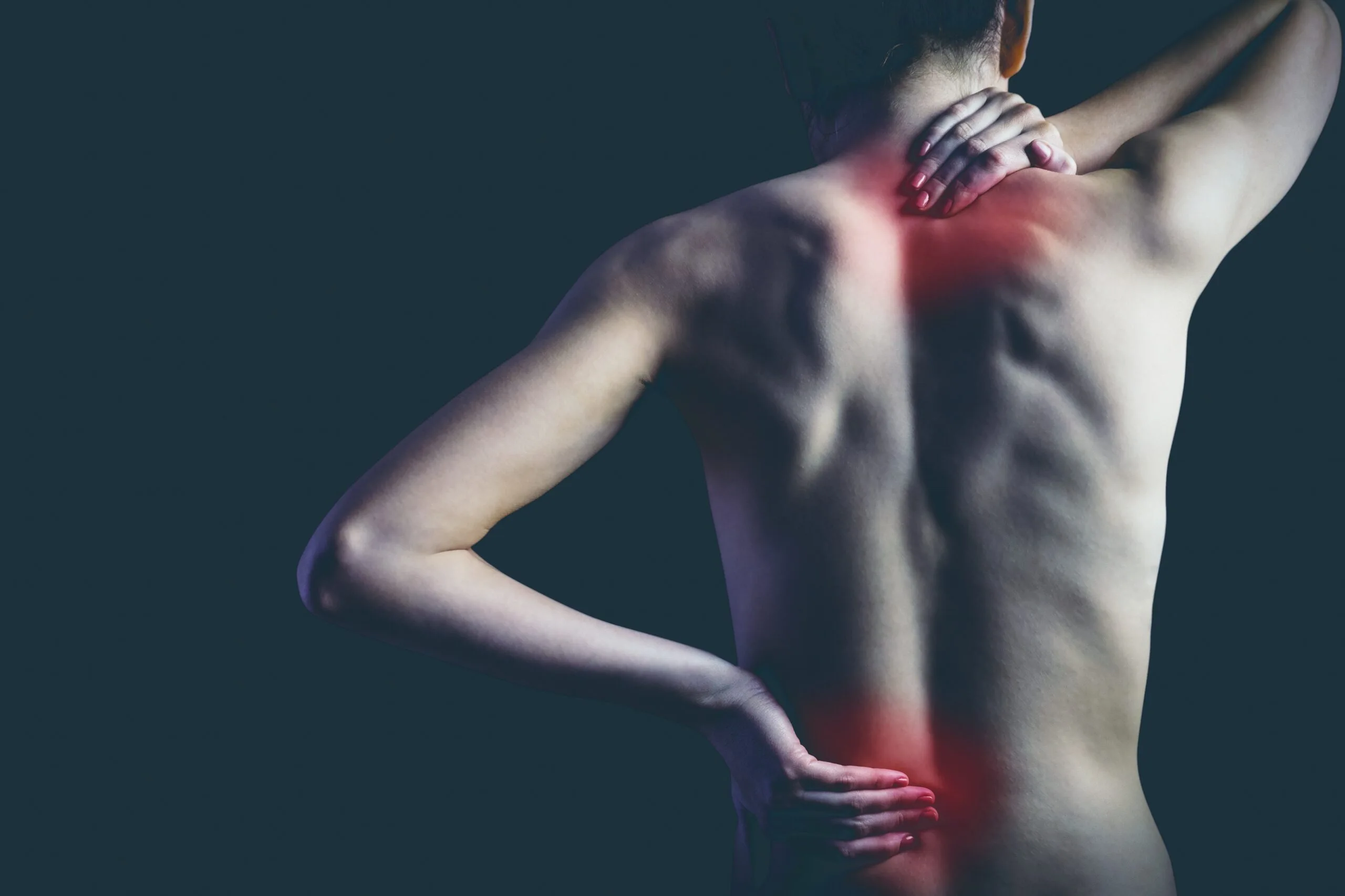 Eine Person ist von hinten abgebildet, die Hände liegen auf Nacken und unterem Rücken, wo rote Markierungen Schmerzen anzeigen. Mit der Expertise der Naturheilpraxis Lübeck könnte Linderung in Sicht sein. Der dunkle Hintergrund betont die Beschwerden entlang der Wirbelsäule.